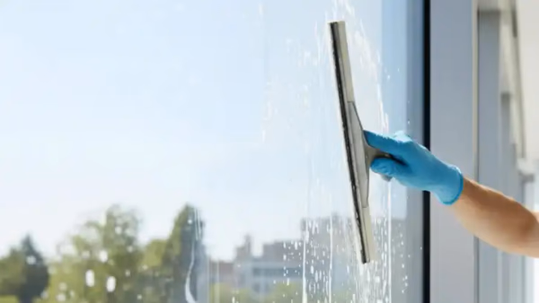 Professional window cleaner using squeegee on large glass window with streak-free results